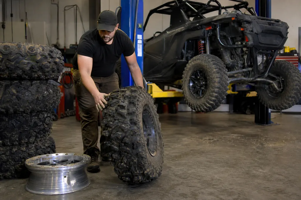 Un homme fait rouler un pneu tout-terrain de SSV dans un atelier de montage