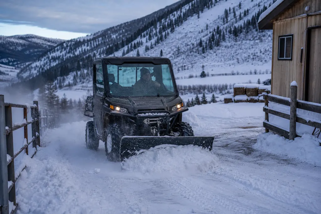 Un SSV à cabine fermée équipé d'une lame déneige une allée de ferme en montagne