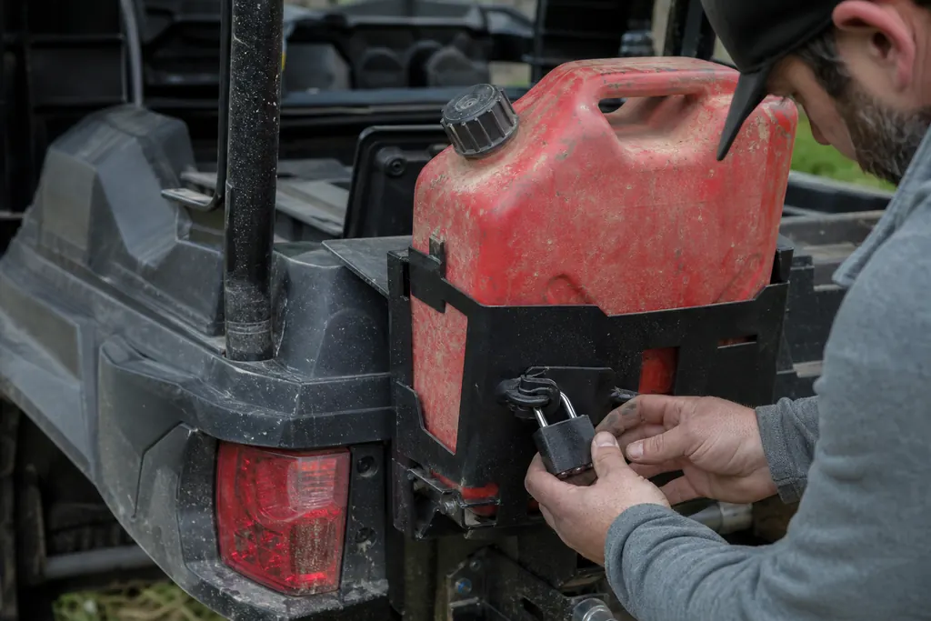 Une main verrouille un jerrican rouge dans son support fixé sur la benne d'un SSV