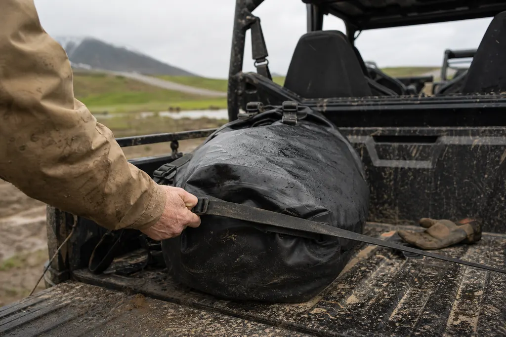Sac étanche arrimé dans la benne boueuse d'un SSV sous la pluie